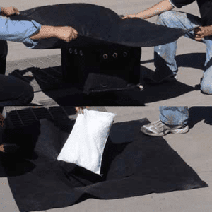 Two people are covering a fire pit with a black blanket, possibly for safety or to extinguish the flames.